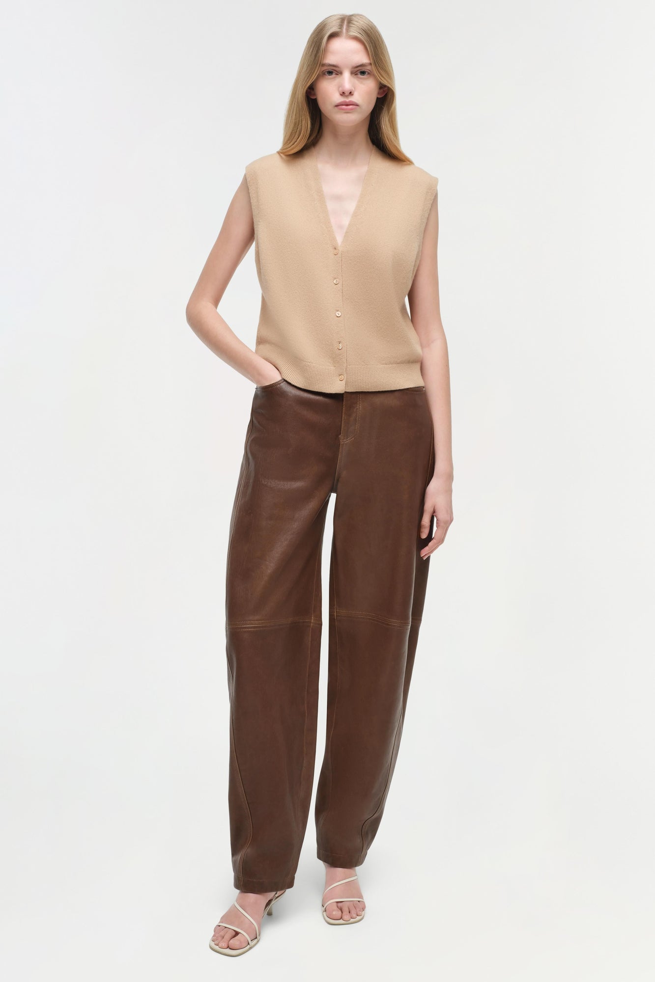 Beige sleeveless cashmere vest with V-neckline and button front on model wearing brown leather pants.