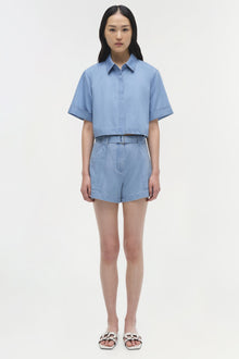 Light blue cropped cotton button-up shirt with short sleeves and collar, displayed on model.