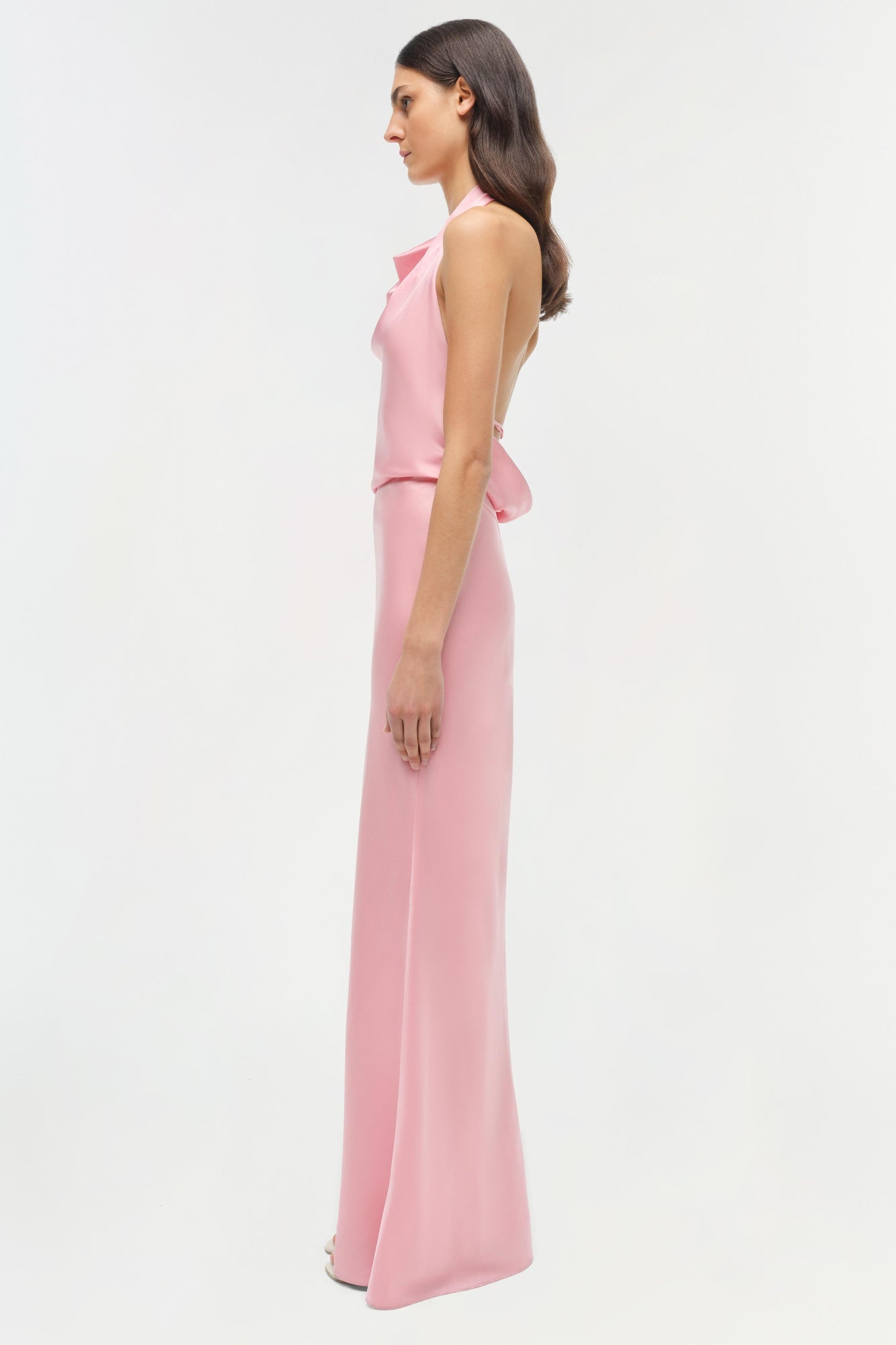 Woman wearing a pink sleeveless satin gown with a ruffled waist detail and floor-length skirt.