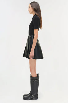 Woman wearing black ribbed knit short-sleeve top with pleated leather skirt and black buckled knee-high boots.