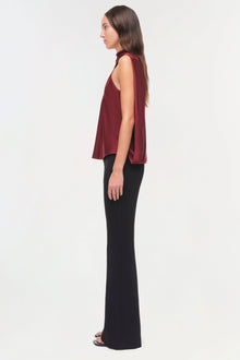 Woman wearing burgundy sleeveless cape top with open back over black pants, shown in profile view.