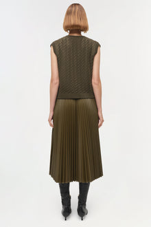 Olive green sleeveless cashmere vest with cable knit pattern, shown from back on model wearing pleated skirt.
