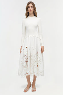 Woman wearing cream knit midi dress with long sleeves and cutout embroidered skirt detail.
