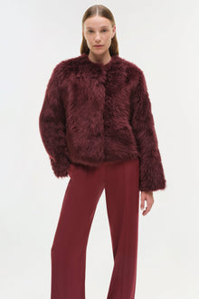 Burgundy shearling jacket with fuzzy texture and crew neckline, styled with matching trousers.