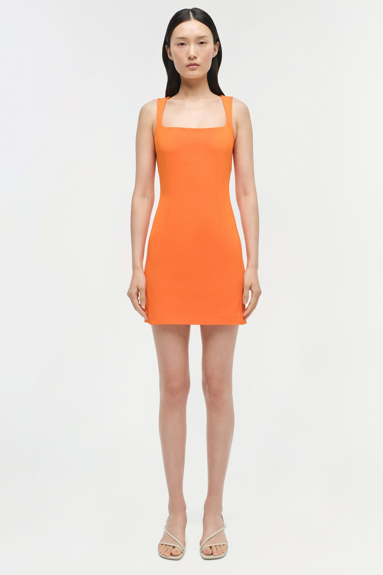 Bright orange sleeveless mini dress with square neckline on model wearing neutral sandals.