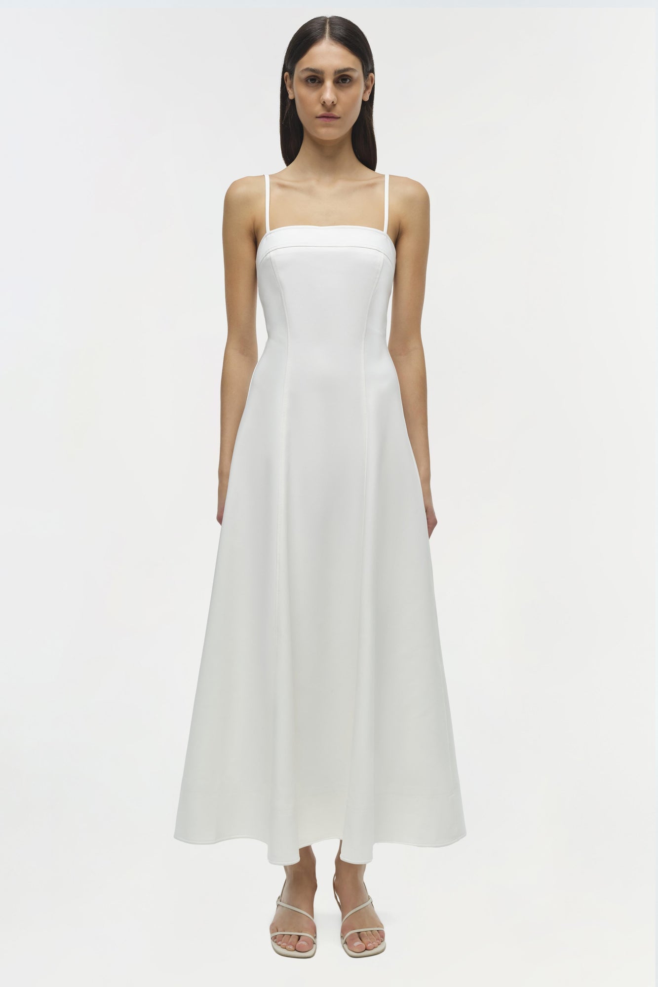 White cotton midi dress with thin straps and A-line skirt, shown on model with white sandals.