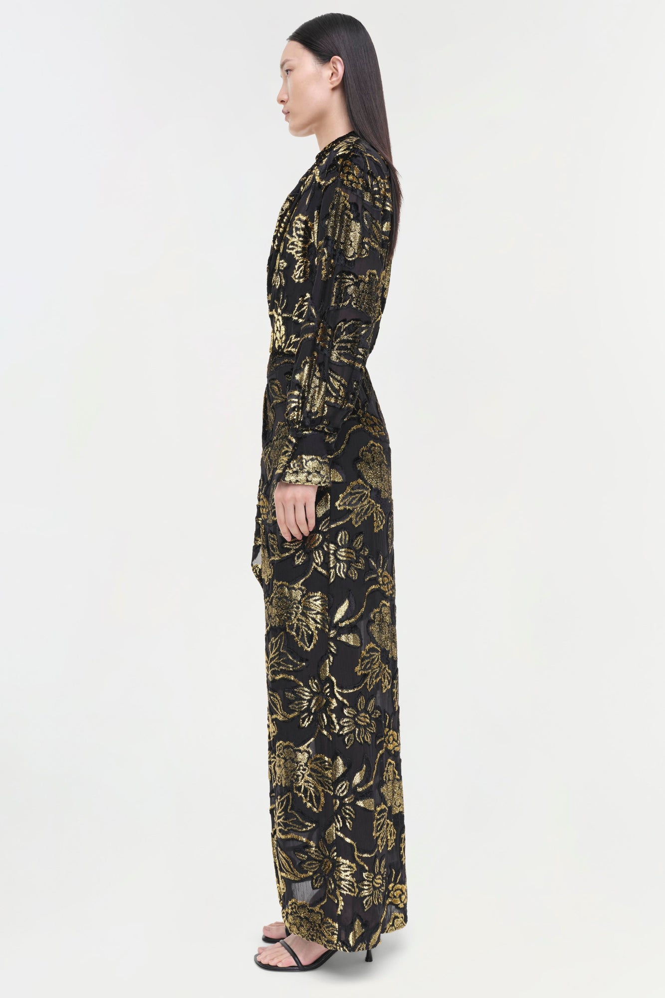 Black long-sleeve gown with gold foliage pattern, fitted silhouette, worn with black sandals.
