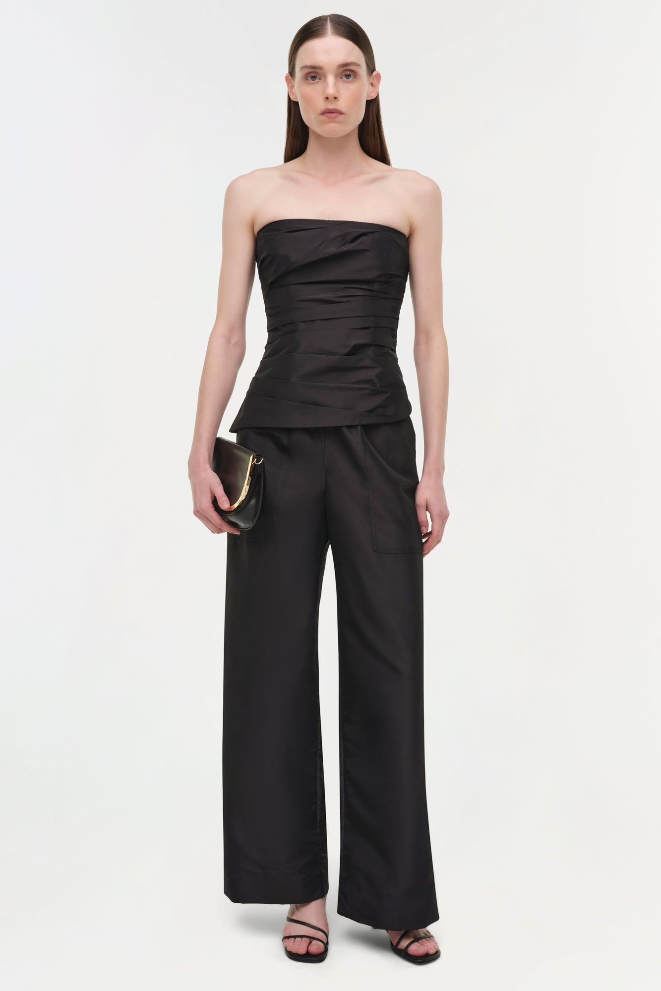 Black strapless bustier top with horizontal ruching paired with wide-leg black pants.