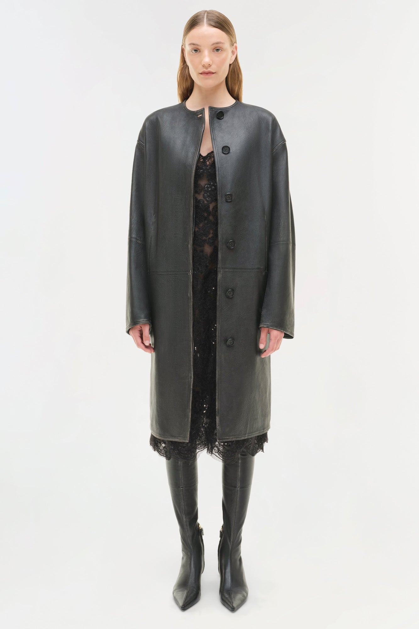 Black leather full-length coat with button front closure worn over black lace dress and matching knee-high boots.