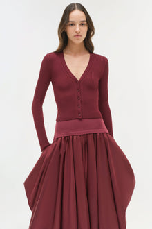 Woman wearing burgundy ribbed knit cardigan with button front paired with midi skirt with gathered taffeta skirt portion.