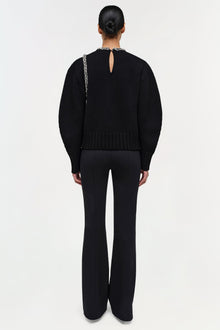 Black pullover with embellished neckline and keyhole back cutout, paired with black flared pants.