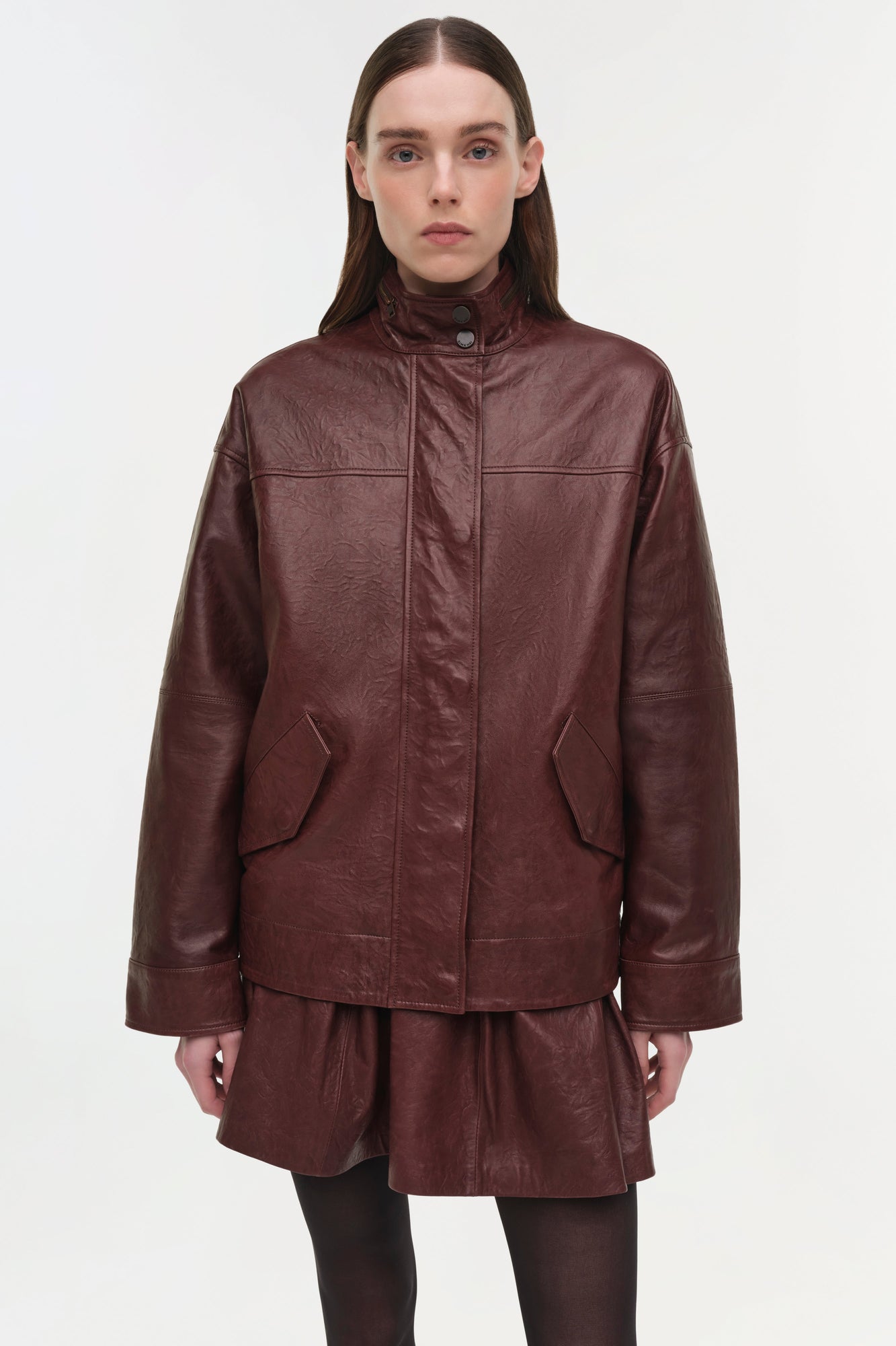 Burgundy leather jacket with high neckline, front snap closure, and patch pockets worn over matching skirt.