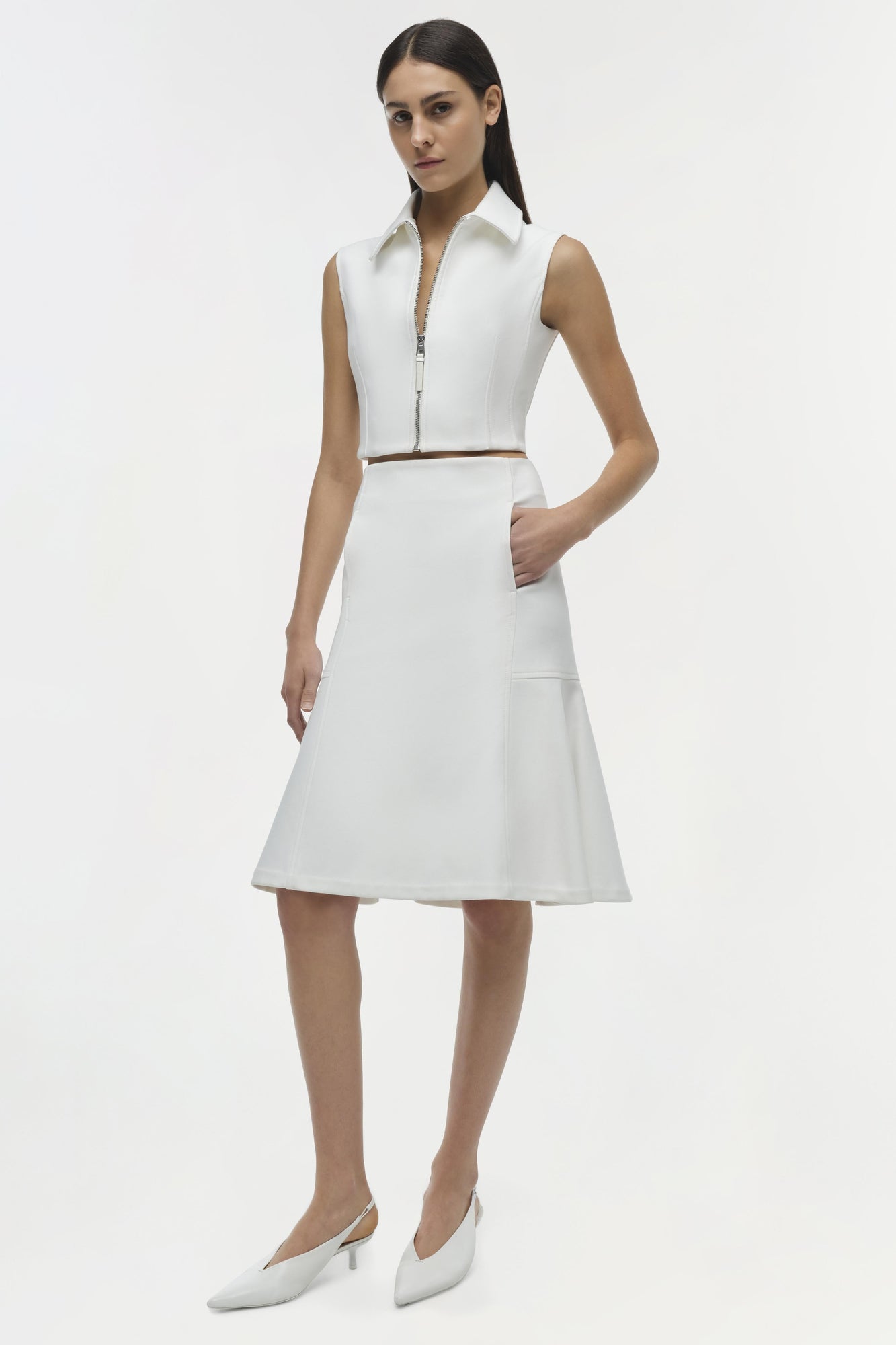White sleeveless shirt dress with collar and front zip, brown belt detail, paired with white pointed kitten heels.