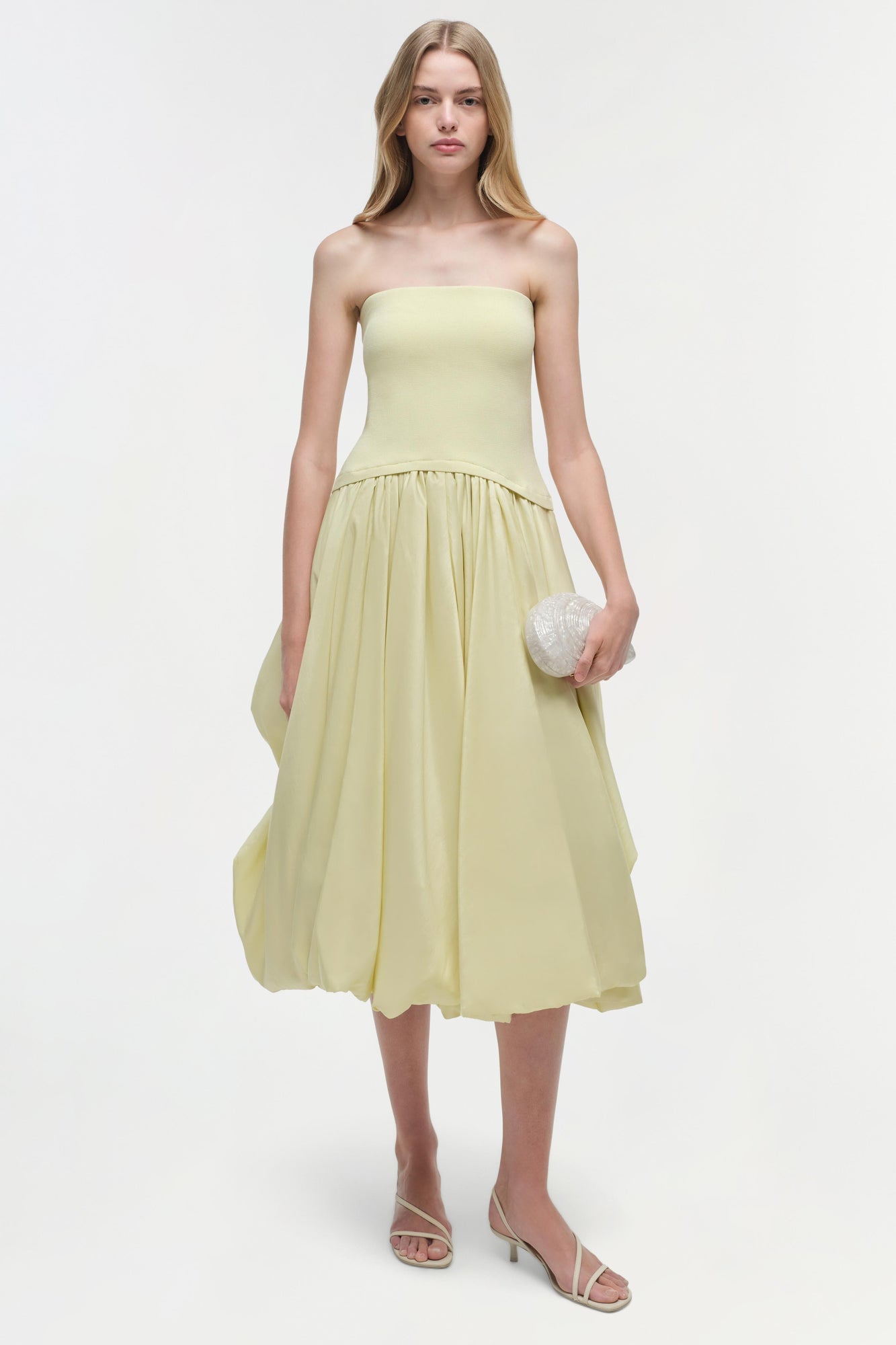 Pale yellow strapless midi dress with fitted bodice and gathered skirt, styled with white beaded clutch and strappy heels.