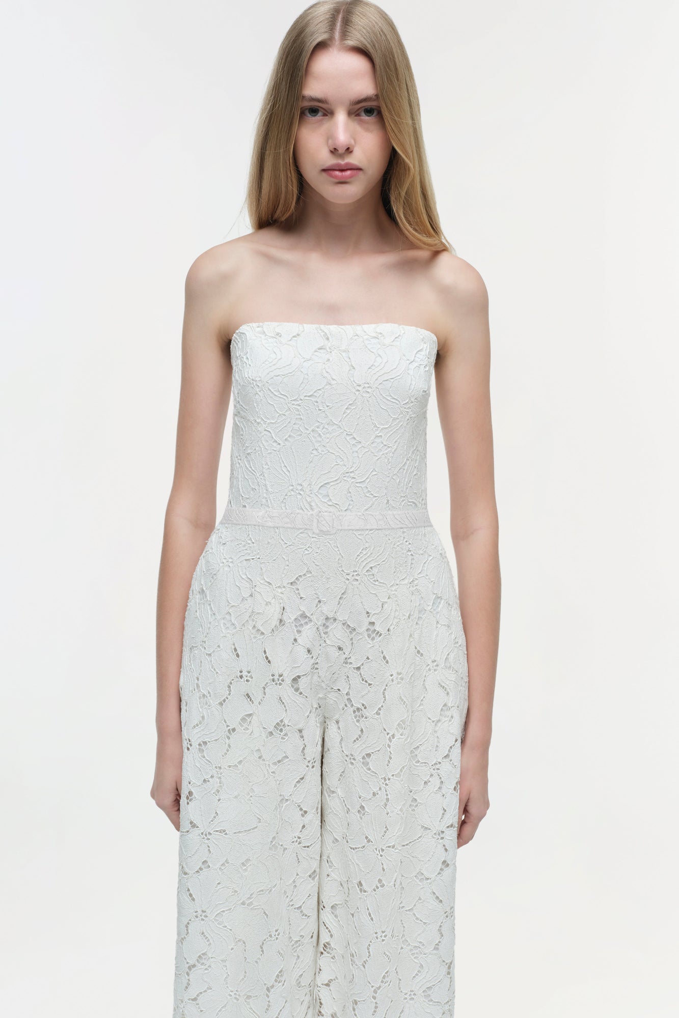 White lace strapless jumpsuit with textured floral pattern and wide-leg pants on model.