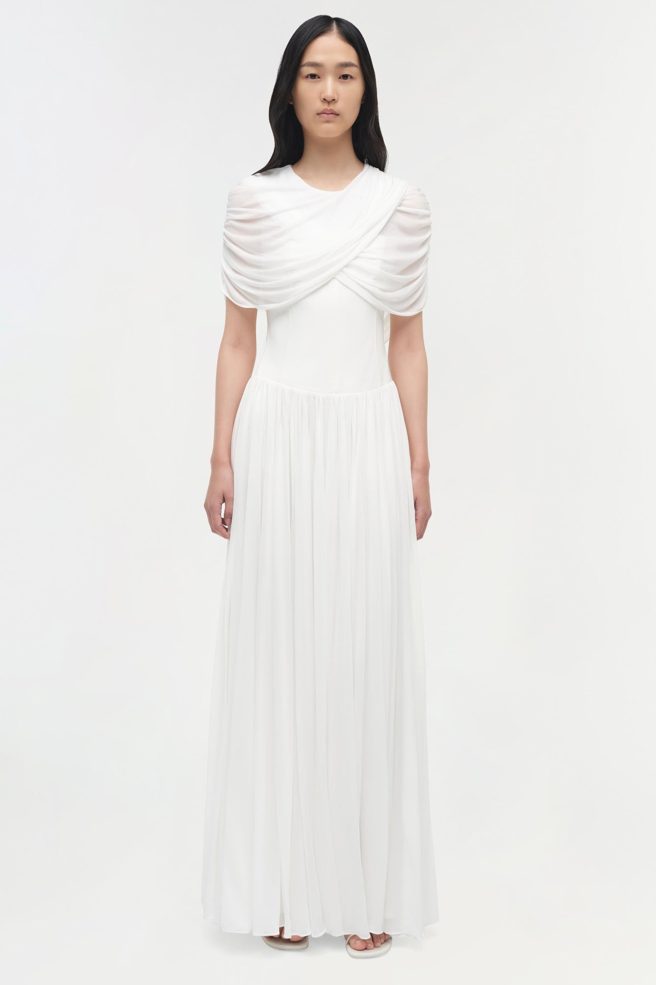 White pleated maxi dress with draped cape overlay across shoulders and short sleeves.