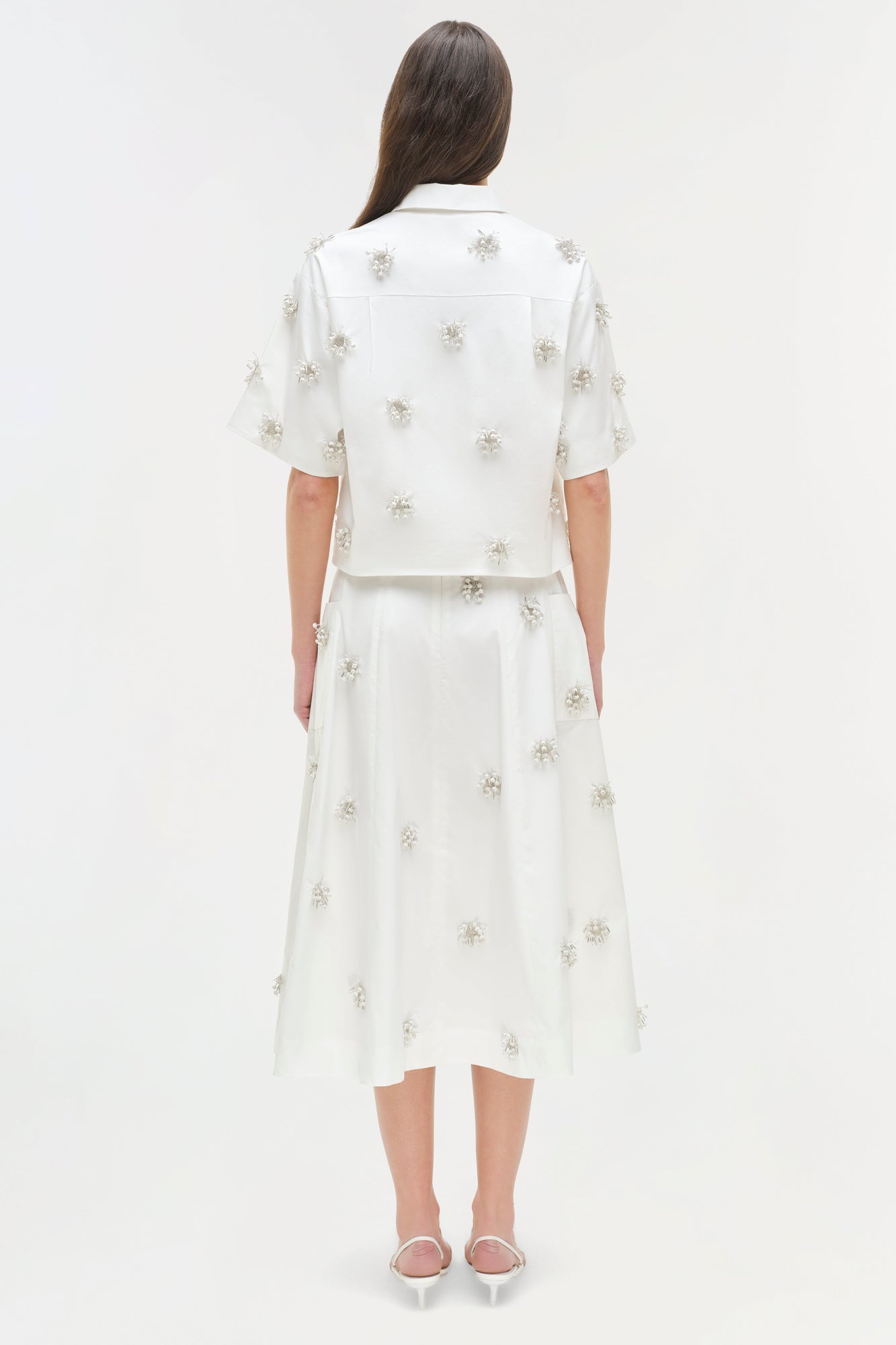 White camp shirt with silver beaded flower embellishments throughout, shown on model from back view.