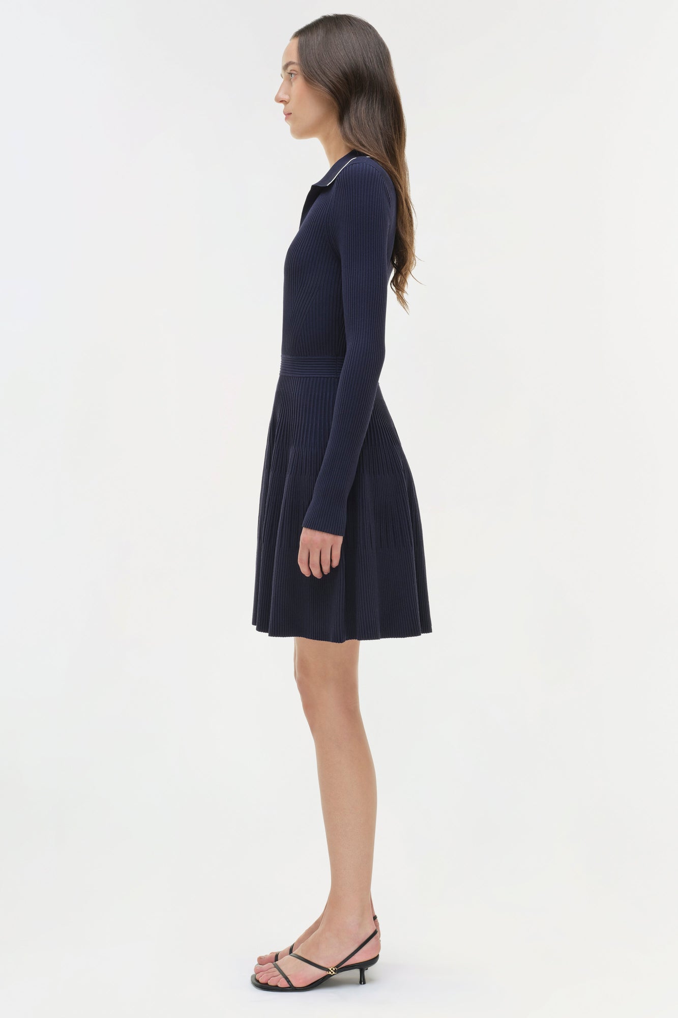 Navy ribbed knit mini dress with long sleeves and pleated skirt, modeled on woman in profile view.