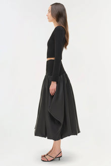 Black cropped knit long-sleeve top with cutout at waist, styled with voluminous mid-calf skirt.