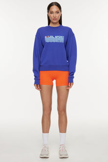 Model wears a royal blue crewneck sweatshirt with the lettering 