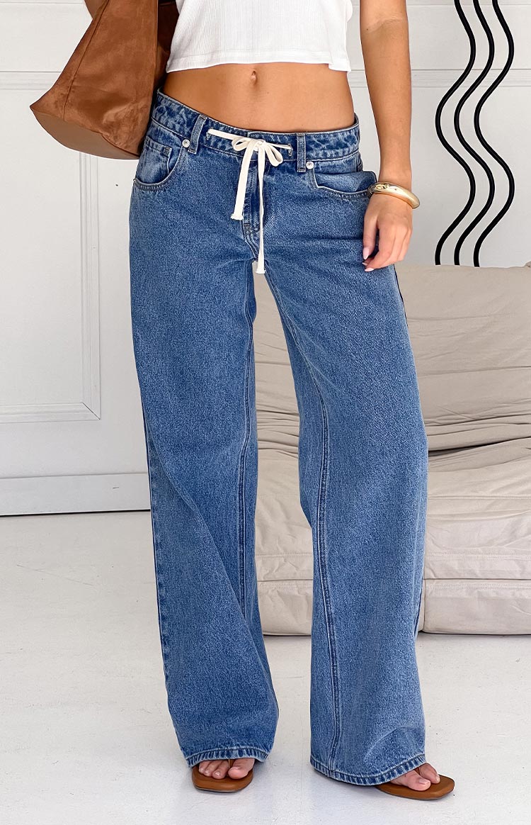 Front view of mid wash denim jeans with a white drawstring tie waist and wide legs