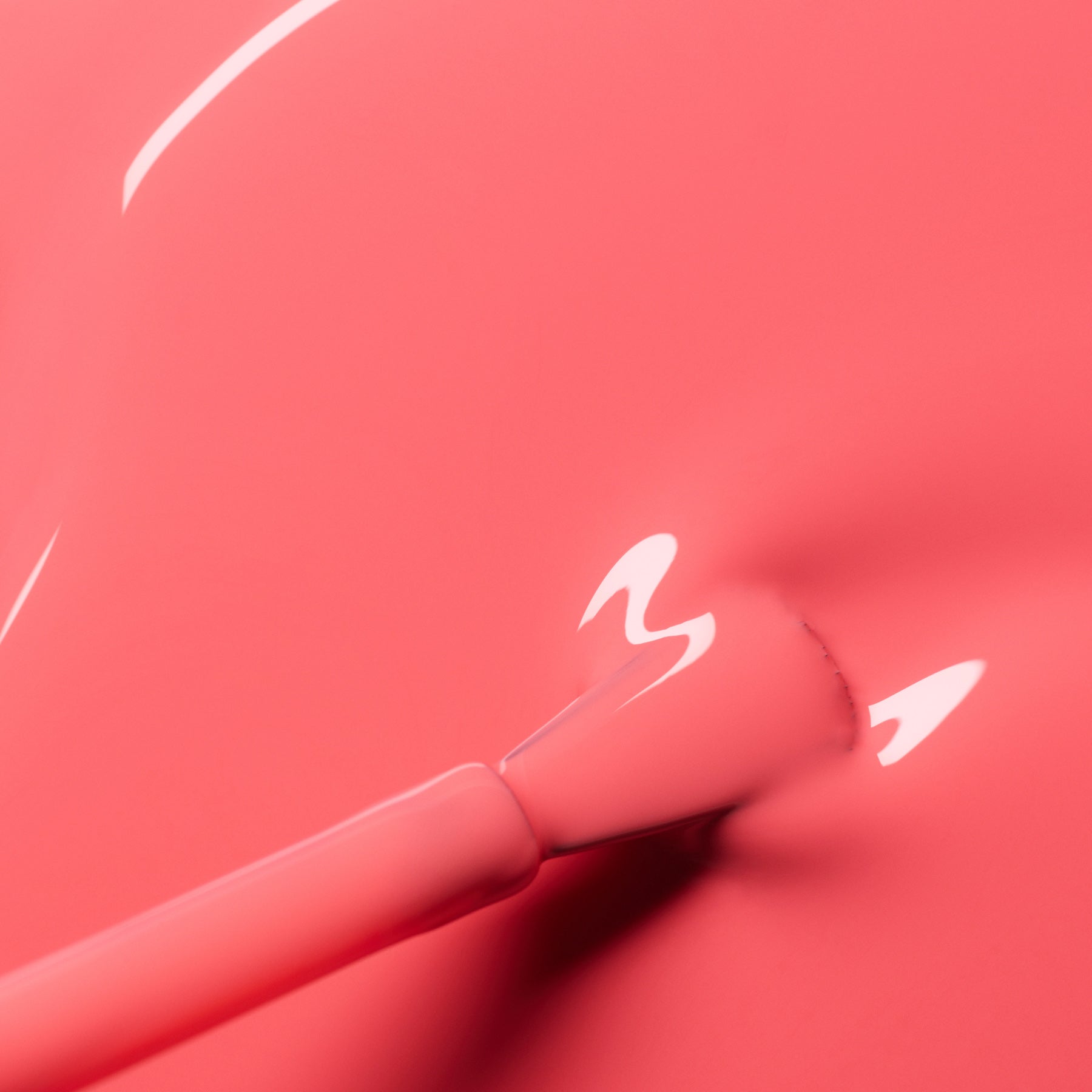 A close-up of a brush applying Manucurist's Capucine gel polish, a glossy coral pink shade with reflections of light shimmering on its smooth, wet surface.