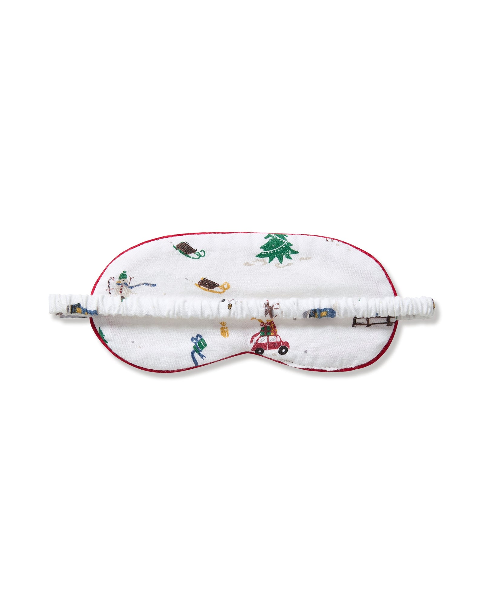 The Kid's Twill Sleep Mask in Holiday Town is a white mask with red trim, decorated with winter scenes of people, a reindeer, a house, a sled, and snowy trees. A small white tag is attached on the right side.