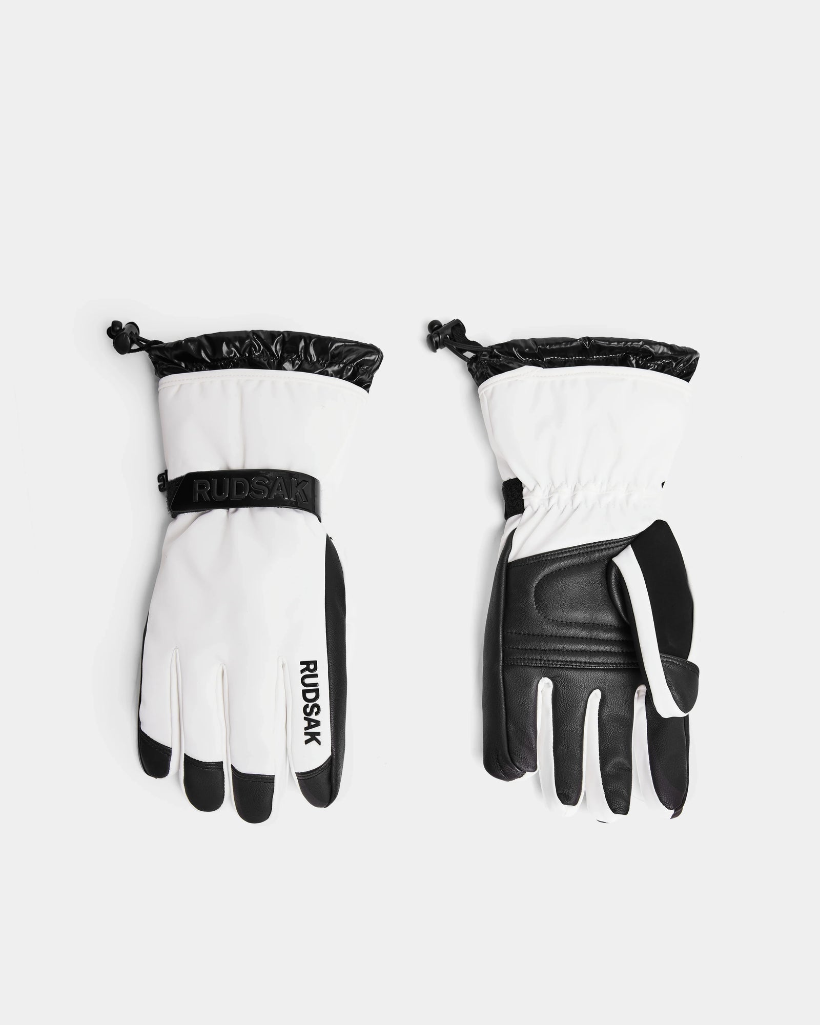 A pair of Rudsak APLEN - 6424505 Optic White ski gloves in white and black, shown front and back with adjustable wrist straps, drawstring cuffs, and waterproof zippers, displayed on a plain light background.