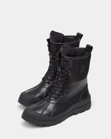 The DAMIEN - M222500 Black by Rudsak are men's high-top winter boots in black, crafted from weather-treated leather with rugged soles, side zippers, stitched panels, and a raised R logo on the outer sides.