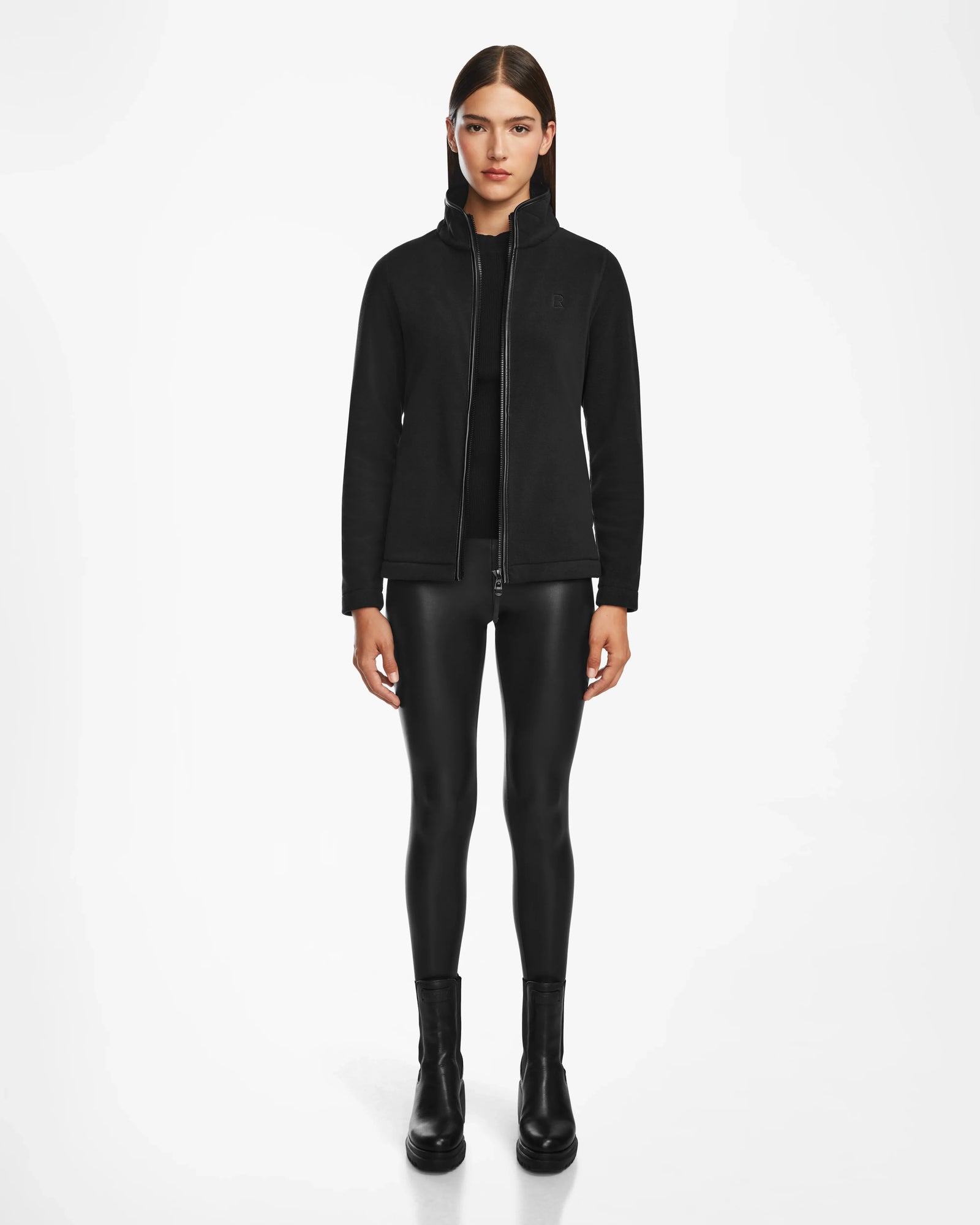 A woman faces forward against a white background, wearing the Rudsak EDITH - 8524617 Black hooded jacket with vegan leather trim, shiny black leggings, and black ankle boots.