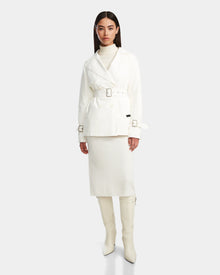 A woman stands against a plain light background wearing the Rudsak ELENOR - 8124707 Iceland trench coat with a shearling collar, a cream turtleneck, matching midi skirt, and white knee-high heeled boots.