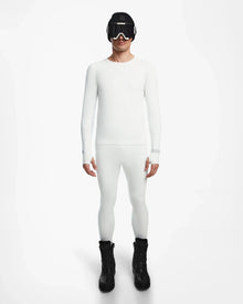 A person stands facing forward, wearing the Rudsak FRANC - 6524541 Iceland fitted white stretch base layer top and matching leggings, paired with black winter boots, ski goggles, and a beanie against a plain white background.