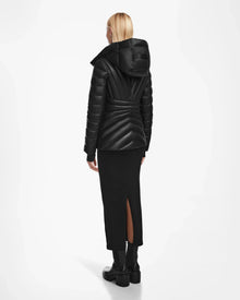 A person with blonde hair, wearing a black Rudsak HANNA X - 8123558 down jacket, a long black skirt with a back slit, and black boots, stands facing away against a white background.