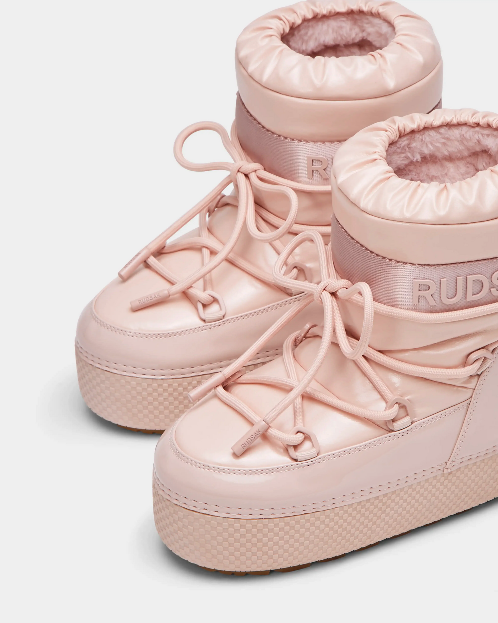 Close-up of HARLOW Y - 1223500 Pastel Pink high-top sneakers with thick soles, elastic ankle cuffs, and decorative laces. These stylish Rudsak winter boots for kids keep feet cozy. Plain white background.