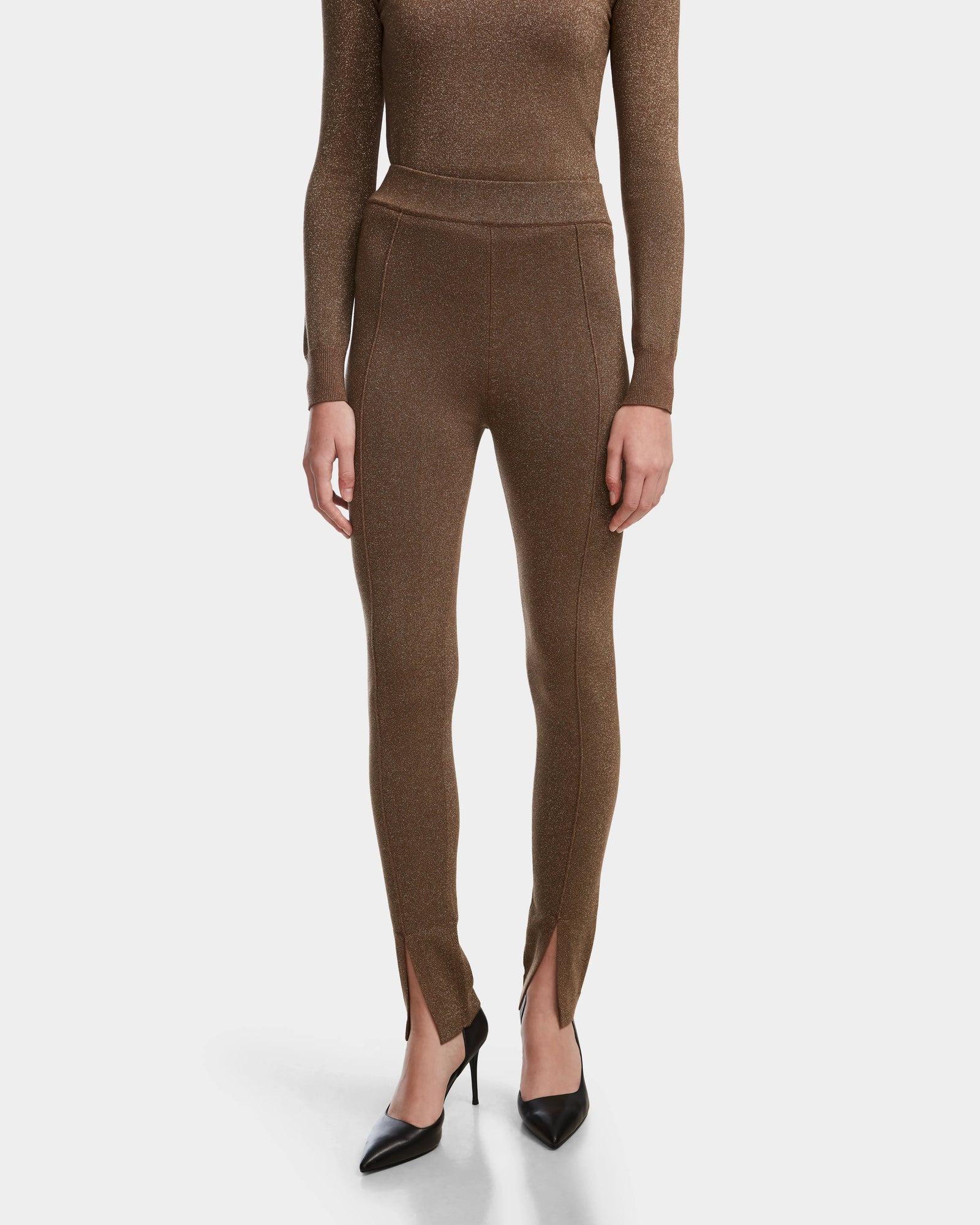 A person models the Rudsak MANSUR - 8524624 Antique Bronze fitted pants and matching top, paired with black pointed-toe heels against a white background—an essential look for any stylish wardrobe.