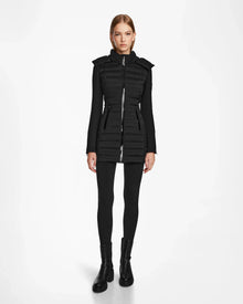 A woman faces forward wearing the RUDSAK MERINA - 8122546 BLACK fitted quilted down jacket with a high collar, paired with black leggings and black ankle boots against a plain white background.