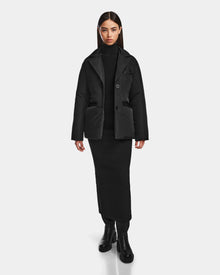 A woman faces forward in a Rudsak PAOLA - 8124547 Black weather-resistant puffer jacket, styled with a black turtleneck, long black skirt, and black boots against a plain white background.