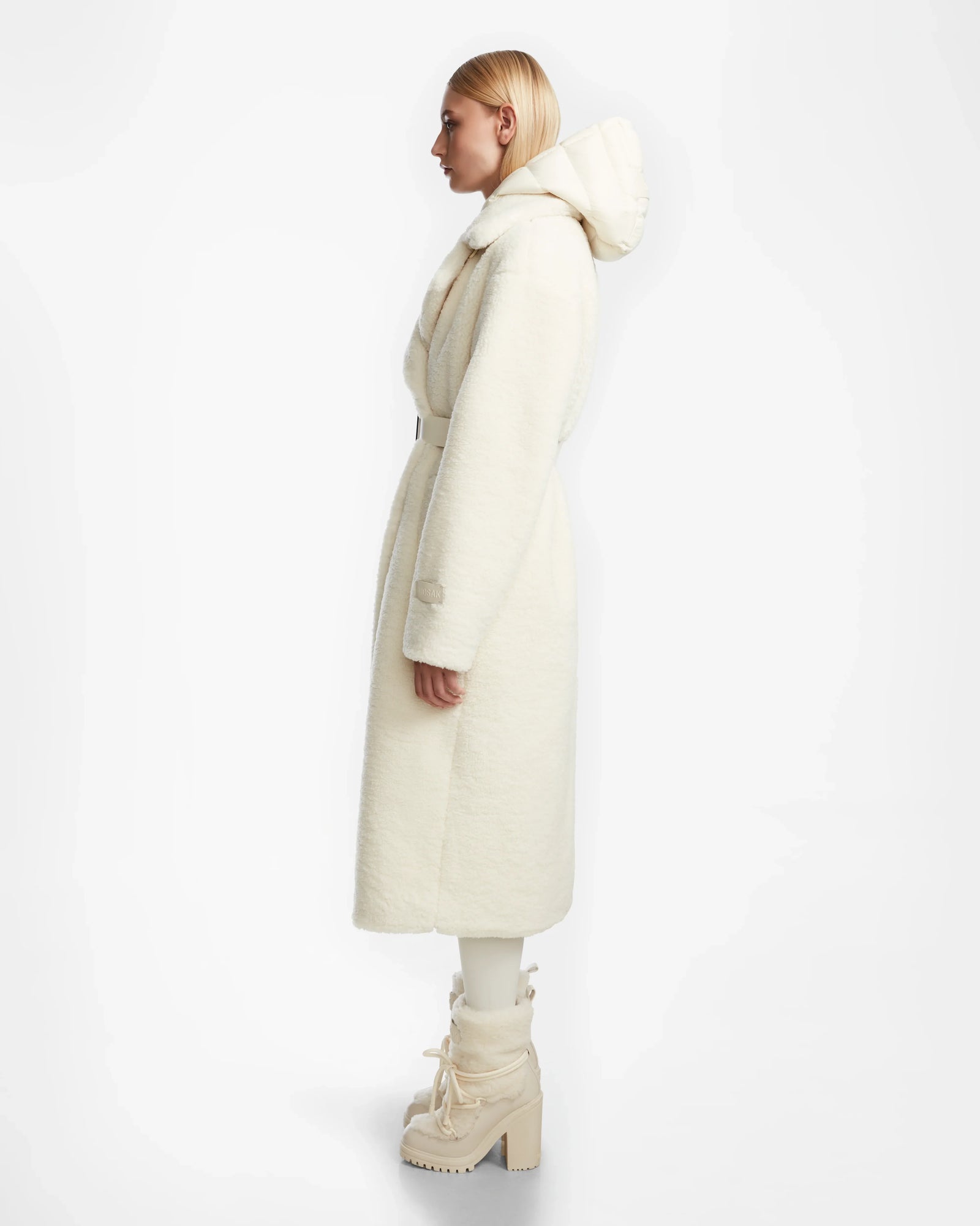 A person with straight blonde hair in profile models the Rudsak TINA - 8123578 Iceland womens trench coat with removable hooded bib and matching off-white high-heeled boots against a plain white background.