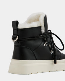 A close-up of the Rudsak ALEXEY L - L225518 Black women’s leather boot featuring black lace-up detail, plush white wool lining, and a thick white sole, shown from the back and side against a plain background.