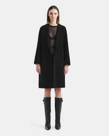 A woman with straight shoulder-length hair and a neutral expression models the Rudsak ARTIS - L125575 Black wool coat with faux fur collar, layered over black pieces, against a plain white background.