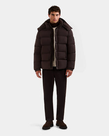 A man faces forward wearing the Rudsak BRAYDEN M-S - M125524 Espresso men's down puffer jacket, dark pants, scarf, and brown shoes, standing against a plain white background.