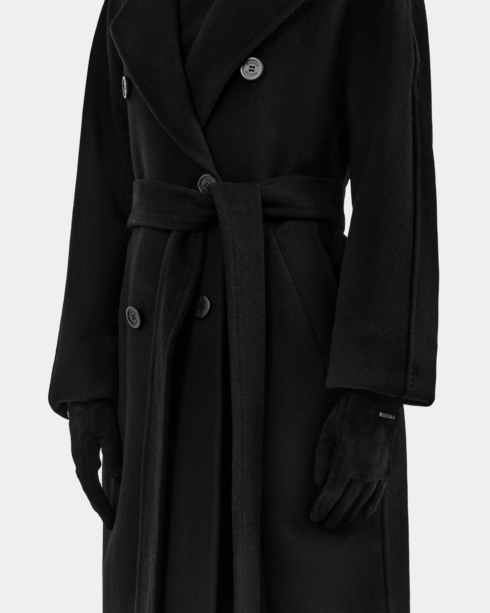 A person wearing the Rudsak FLORA - L425542 Black long coat with a belt and wool-cashmere lined gloves, shown from shoulders to knees against a plain background.