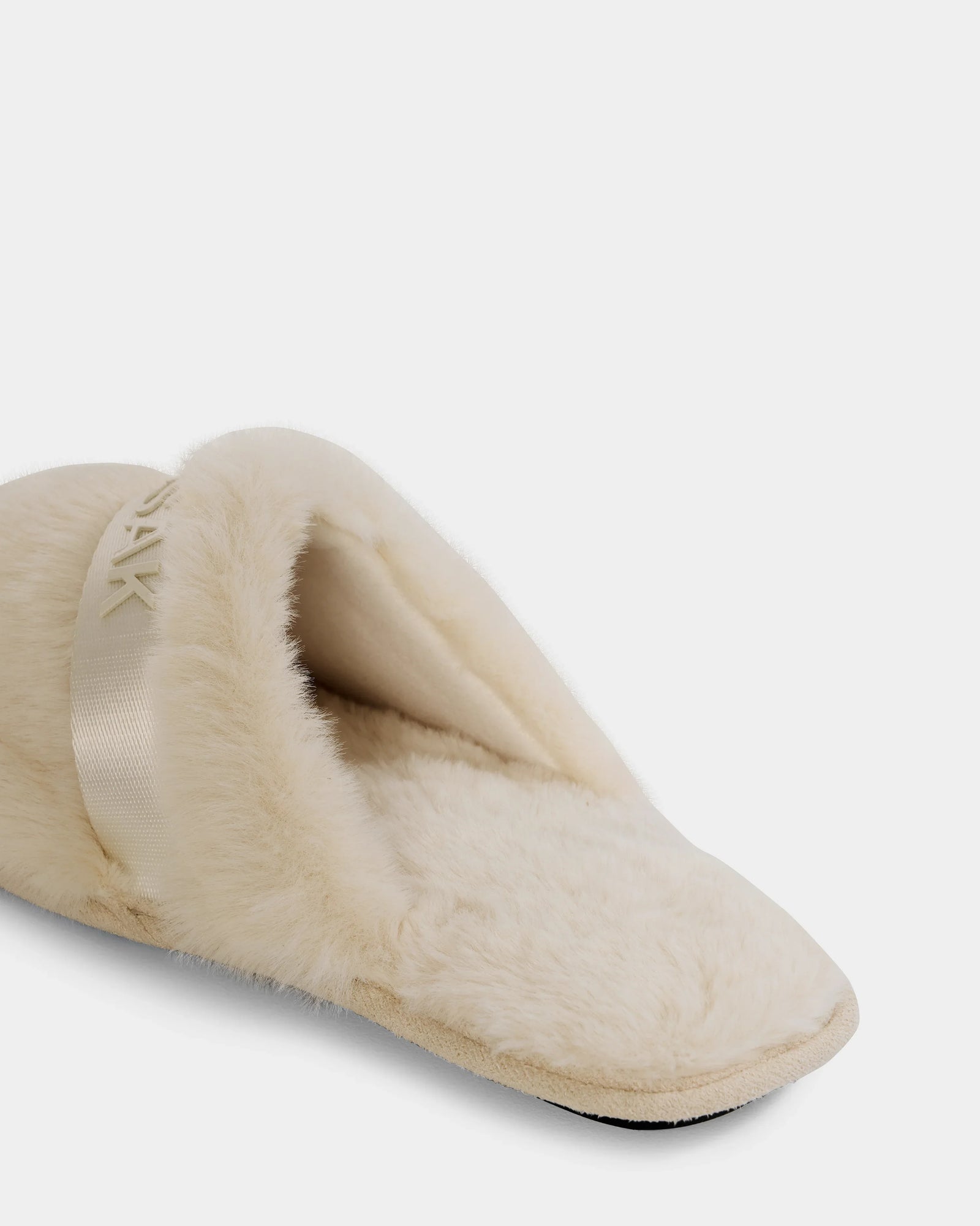 A close-up of the FLUFF - L223509 Cream women’s faux-fur slipper by Rudsak, featuring plush material, a satin band detail, and non-slip traction for cozy downtime—all shown on a white background.