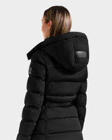 A woman with straight, shoulder-length hair models the Rudsak FRIDA M-L - L125608 Black down coat with a detachable hood, sleeve patch, and branded hood label, shown from the back against a plain light gray background.