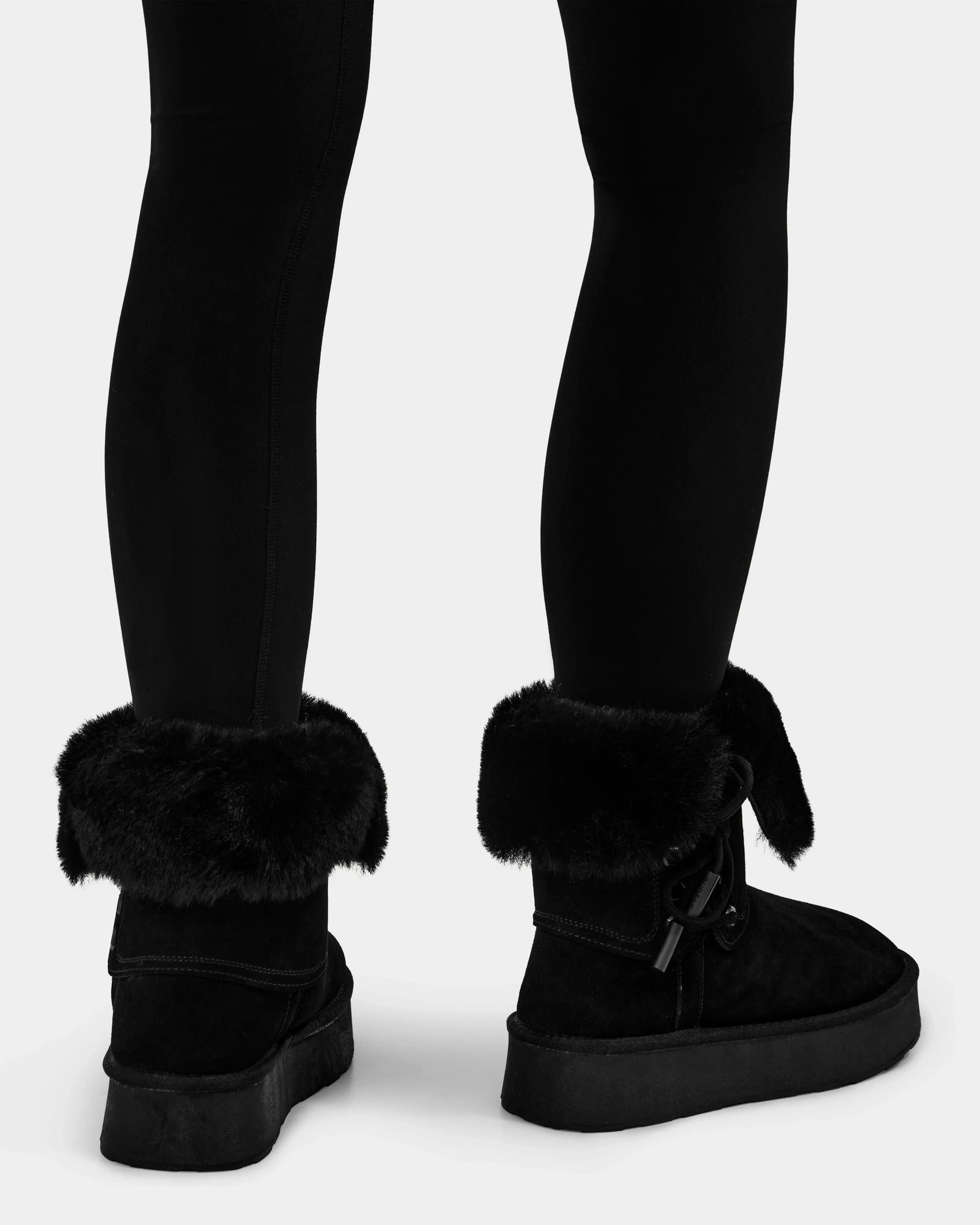 A person wearing black leggings and Rudsak INESA - L225026 Black women’s suede platform boots with a lightweight sole, shown from the calves down, standing on a white background.