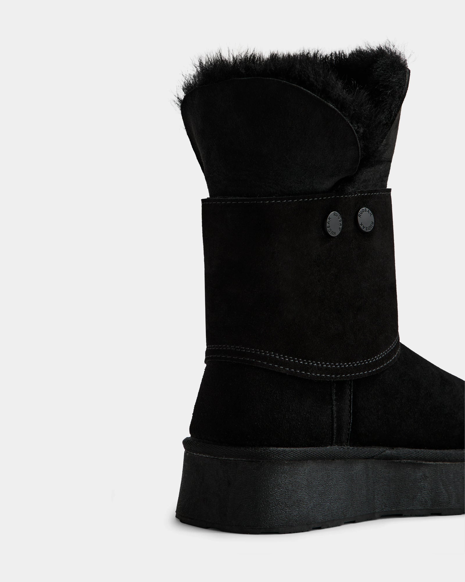 A close-up of the Rudsak INESA - L225026 Black women’s suede platform boot with lace-up front, black fur lining, decorative buttons, and visible stitching, shown on a plain white background.
