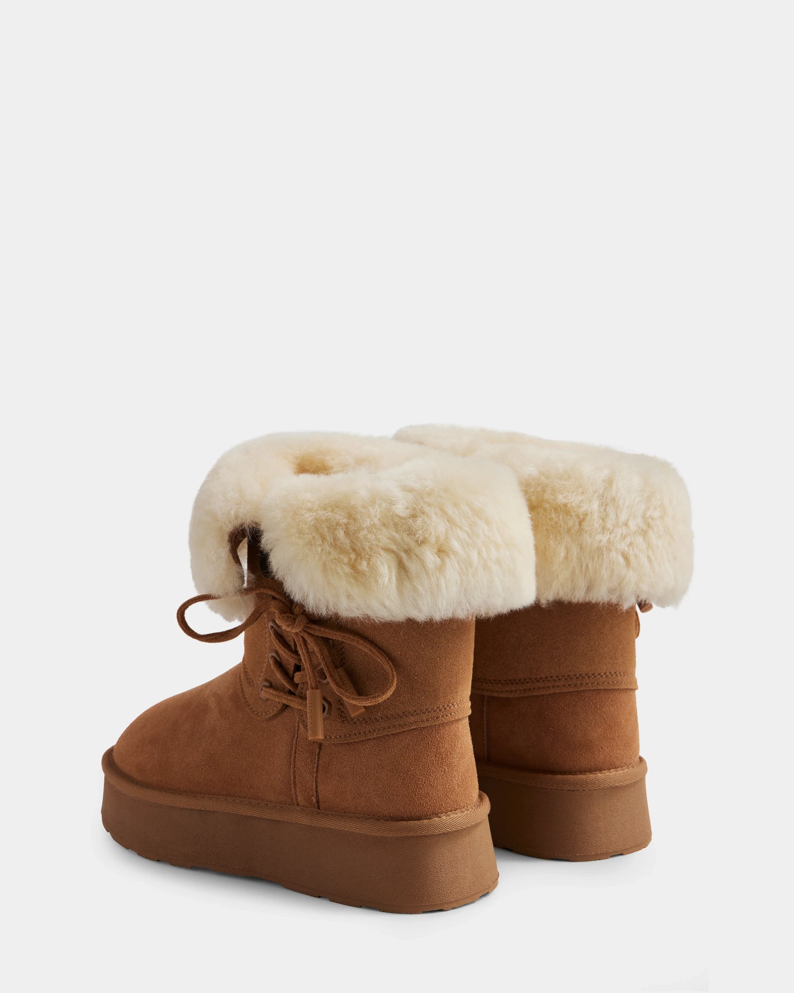 The INESA - L225026 Tan by Rudsak are women’s brown suede platform ankle boots with tan rubber soles and folded-over wool-lined cuffs. One cozy winter boot faces forward, the other is angled slightly back.