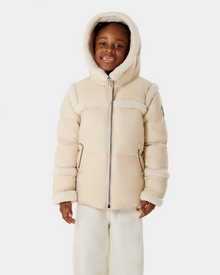 A young child models the Rudsak JULIANA K - K125550 Vanilla, a cream hooded winter jacket with faux fur trim and matching light pants, smiling against a plain white background.