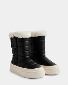 The KATHIE - L225516 Black by Rudsak is a pair of black quilted vegan leather women’s mid boots with white faux fur lining, thick cream soles, side zippers, and two top buttons, shown on a plain light background.
