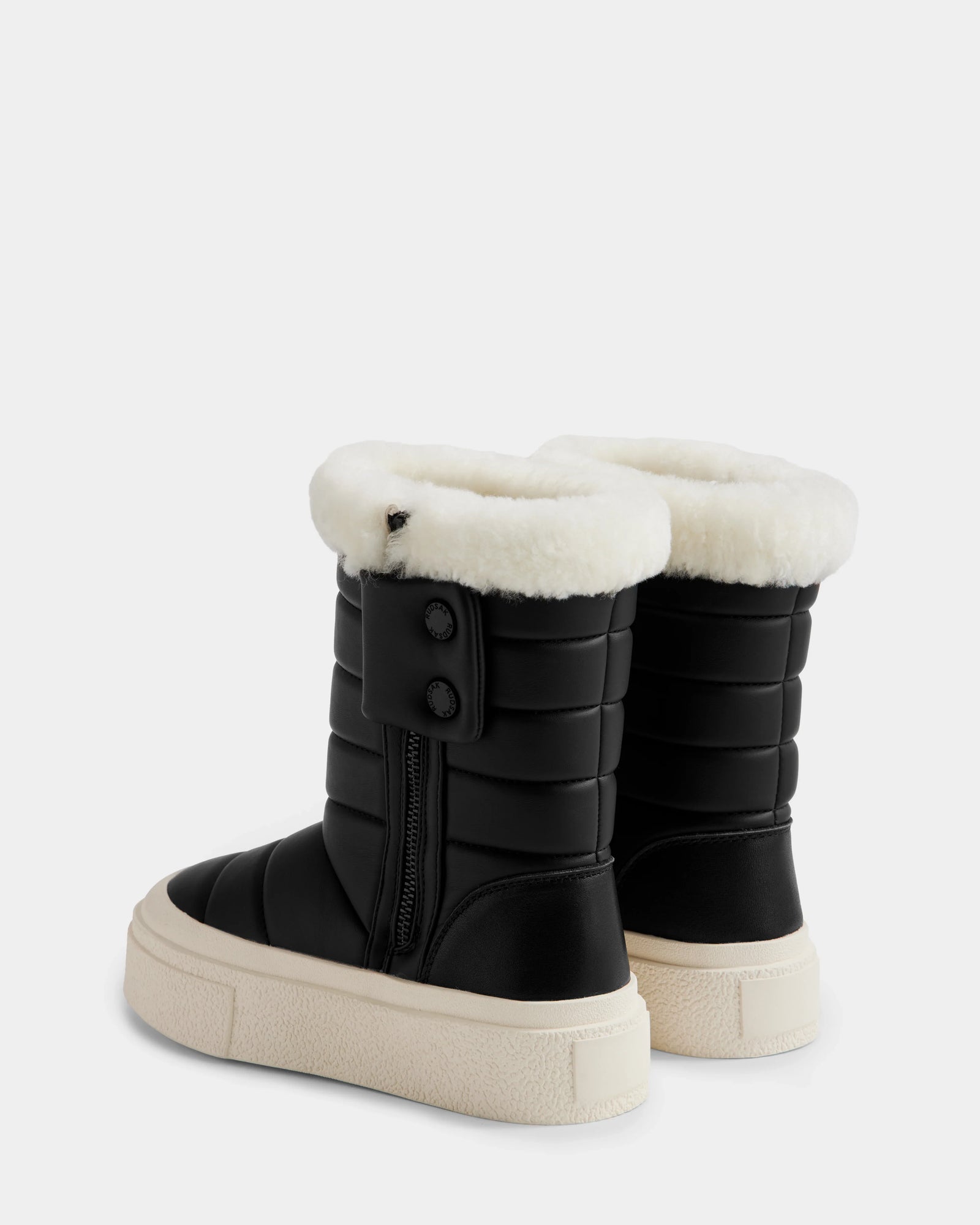 The KATHIE - L225516 Black women's mid boots by Rudsak feature black quilted vegan leather, thick white faux fur lining, side zippers, and light rubber soles, shown against a plain white background.